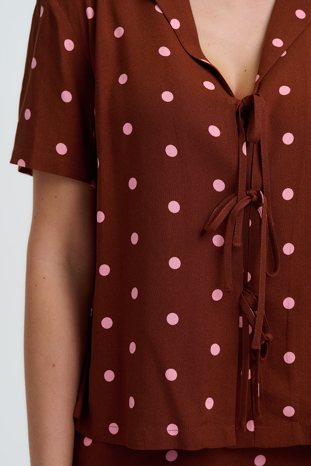Brown blouse with pink polka dots and a tie detail on a white background