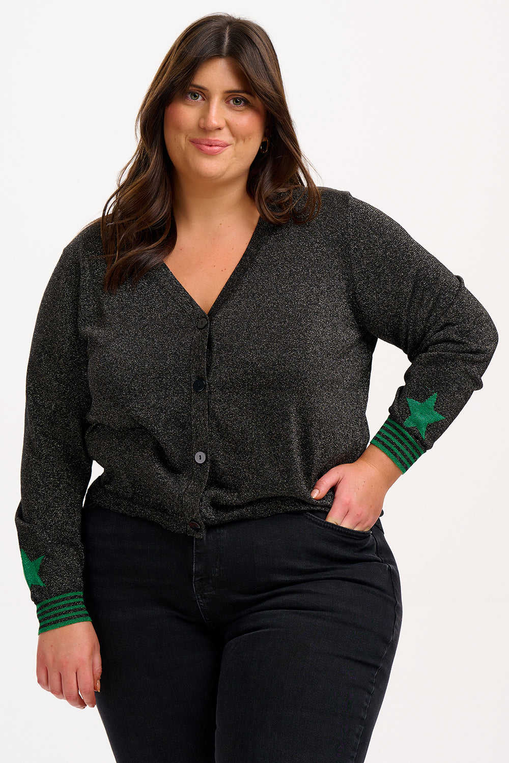 A woman wearing a black long-sleeve cardigan with green stripes and stars on the sleeves, paired with black trousers.
