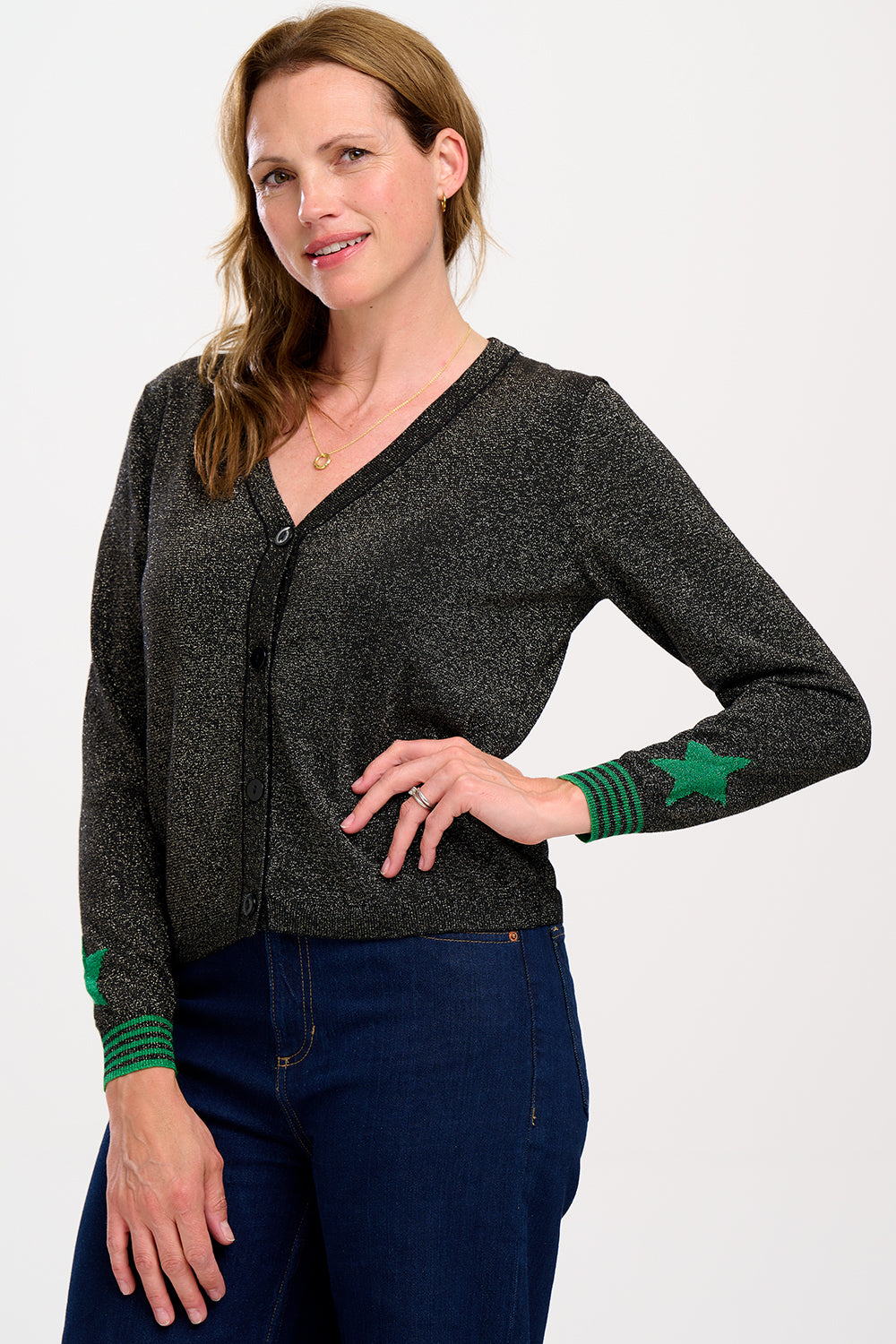 A woman wearing a black long-sleeve cardigan with green stripes and stars on the sleeves, paired with black trousers.