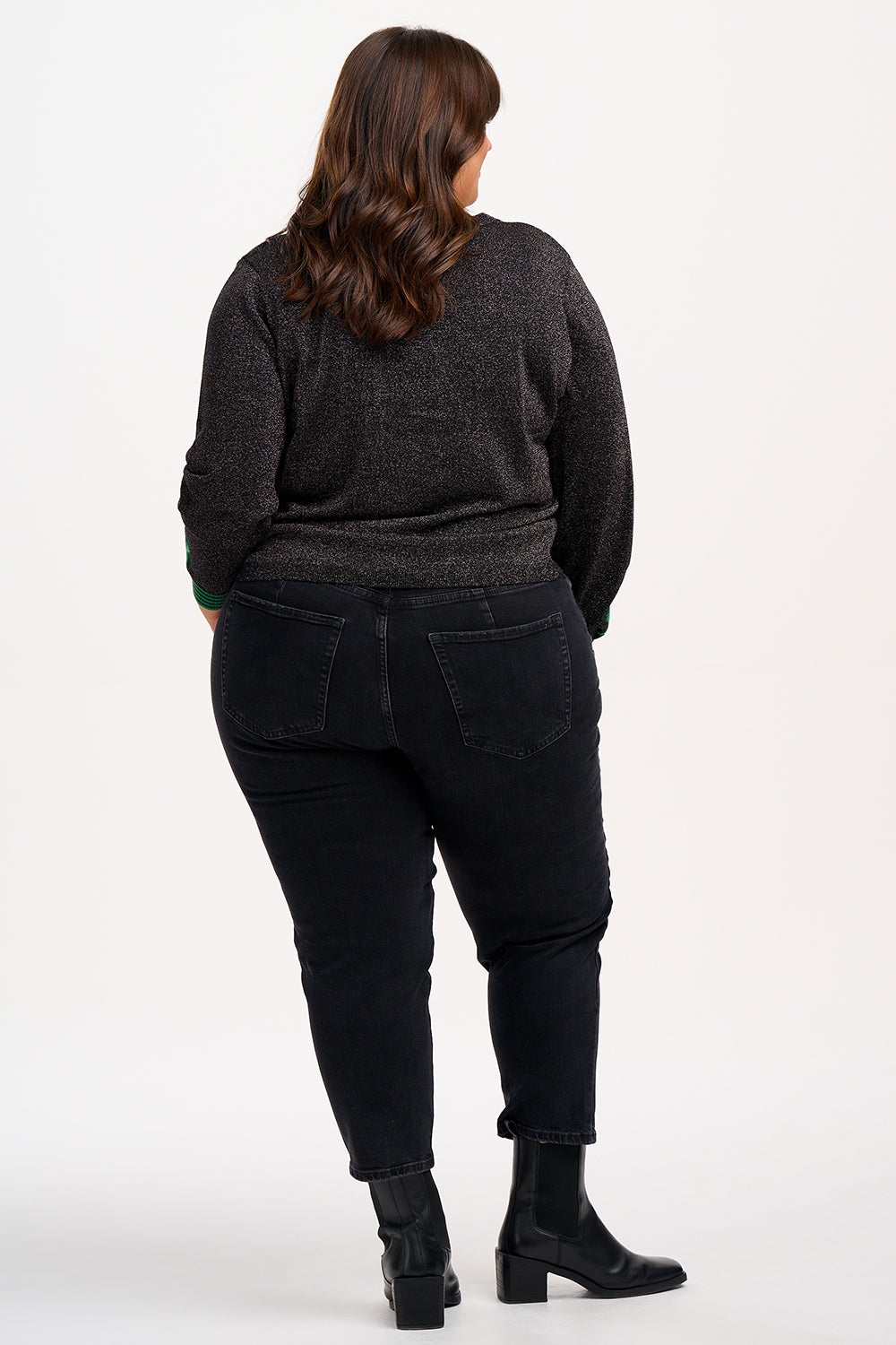 A woman wearing a black long-sleeve cardigan with green stripes and stars on the sleeves, paired with black trousers.