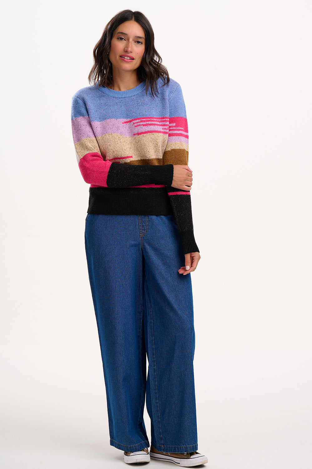Woman wearing a colorful sweater and blue jeans on a white background