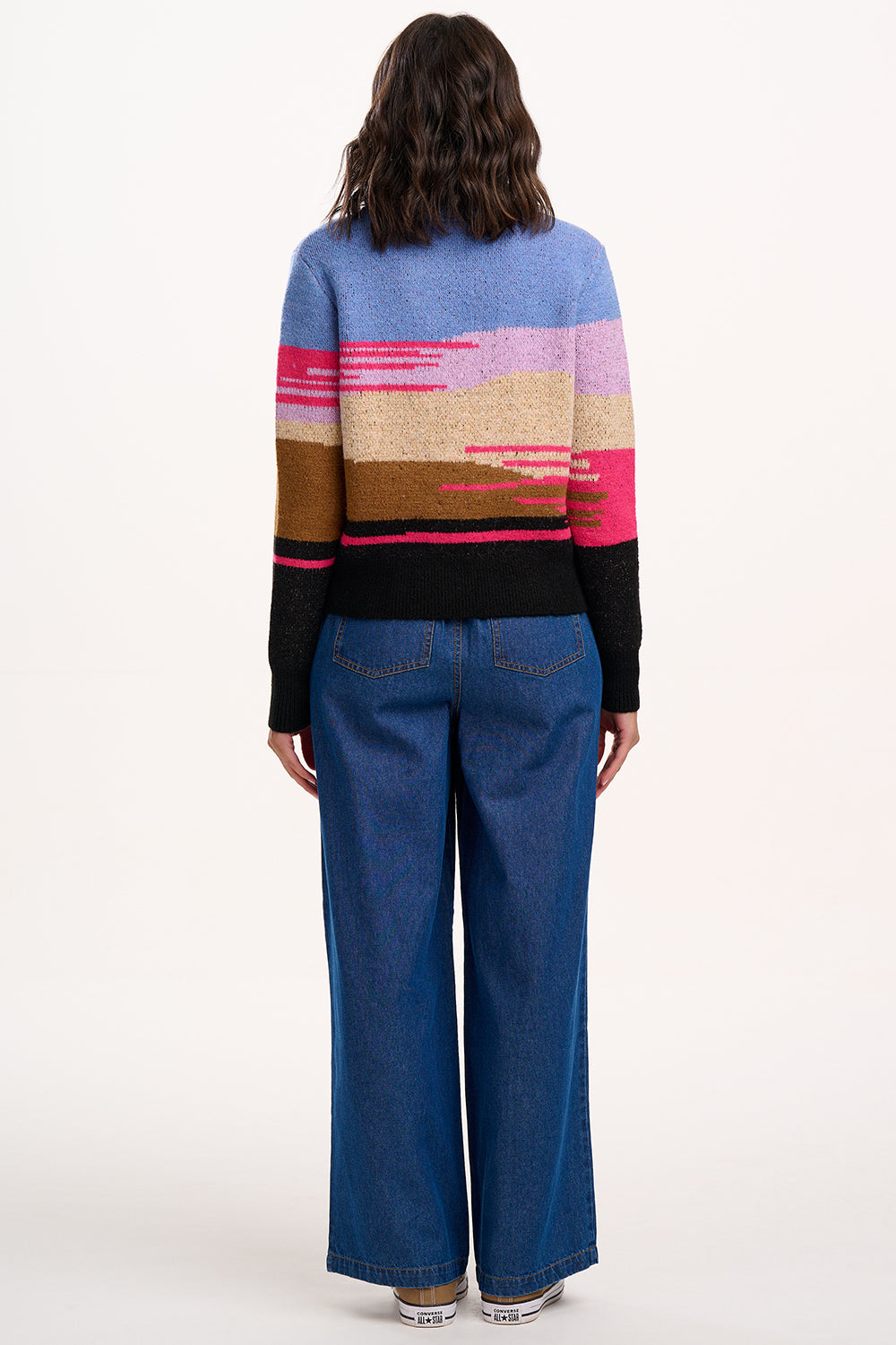 Person wearing a colorful sweater and blue jeans on a white background