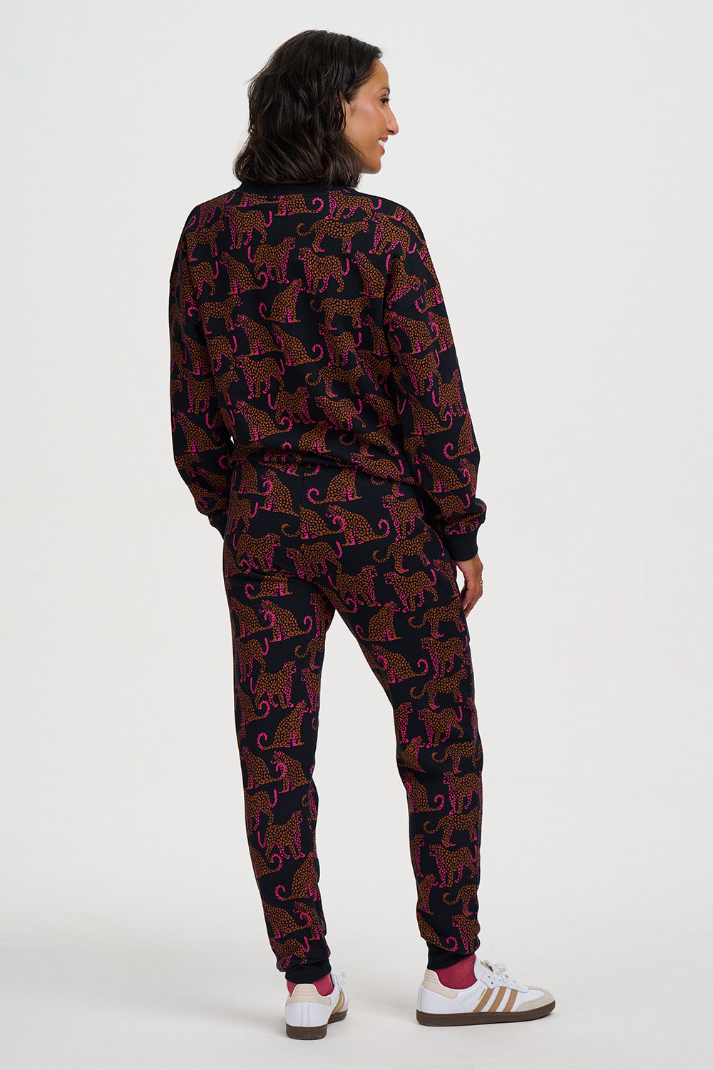 A woman shown from the back wearing a matching long-sleeve sweatshirt and jogger pants set with an allover dark elephant print, paired with white sneakers, against a plain light gray studio background.