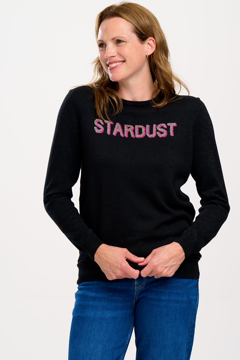 A woman wearing a long sleeve black jumper with the text 'STARDUST' on the front.