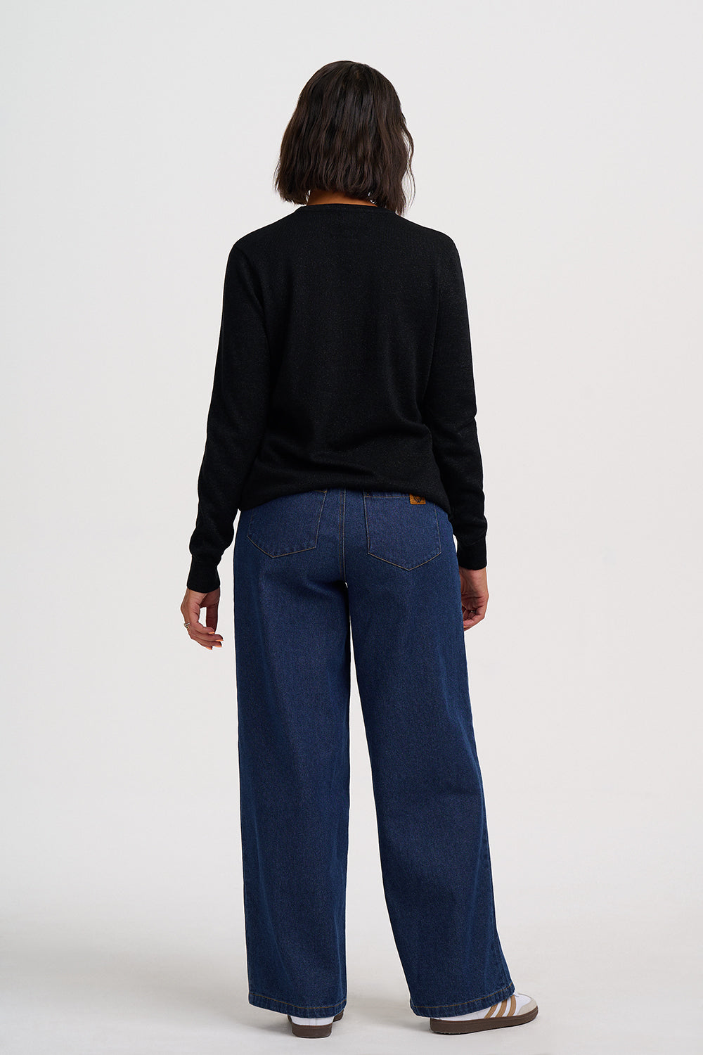 A model shown from the back wearing a black long-sleeve top and dark blue wide-leg jeans, standing against a plain white studio background.