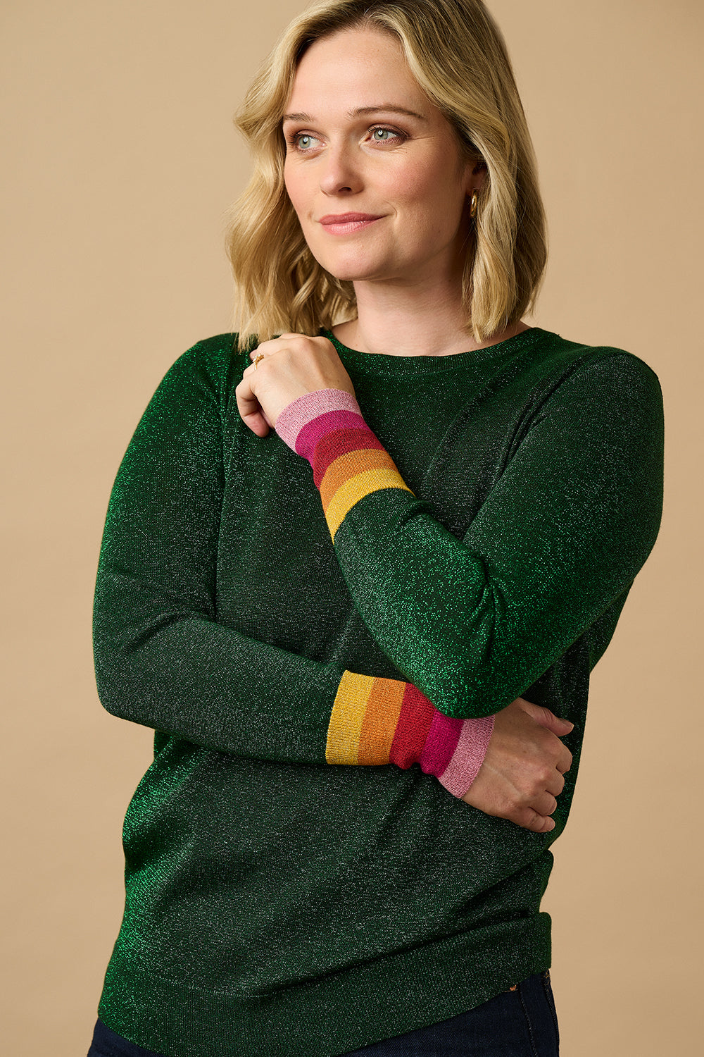 A woman wearing a green crew neck jumper with colorful striped cuffs, paired with blue jeans.