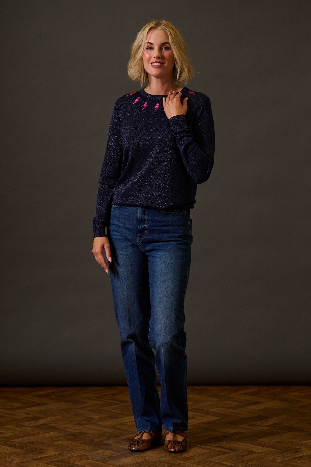 Woman wearing a dark sweater and blue jeans against a plain background