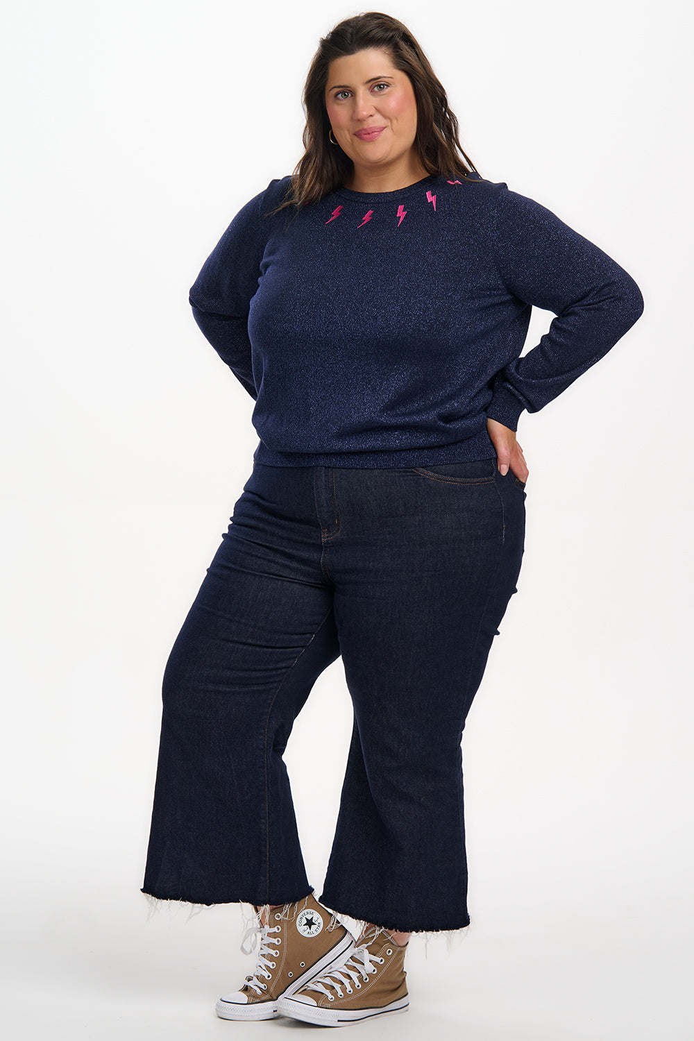 Person wearing a navy sweater and jeans with Converse shoes on a white background