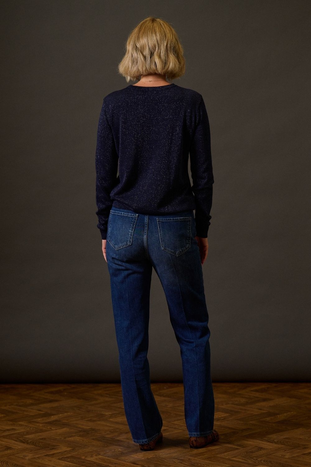 Person wearing a dark blue sweater and jeans standing against a plain background