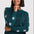 A woman wearing a dark teal knit sweater with white star patterns on the sleeves and body, paired with dark blue jeans, photographed against a light gray studio background.