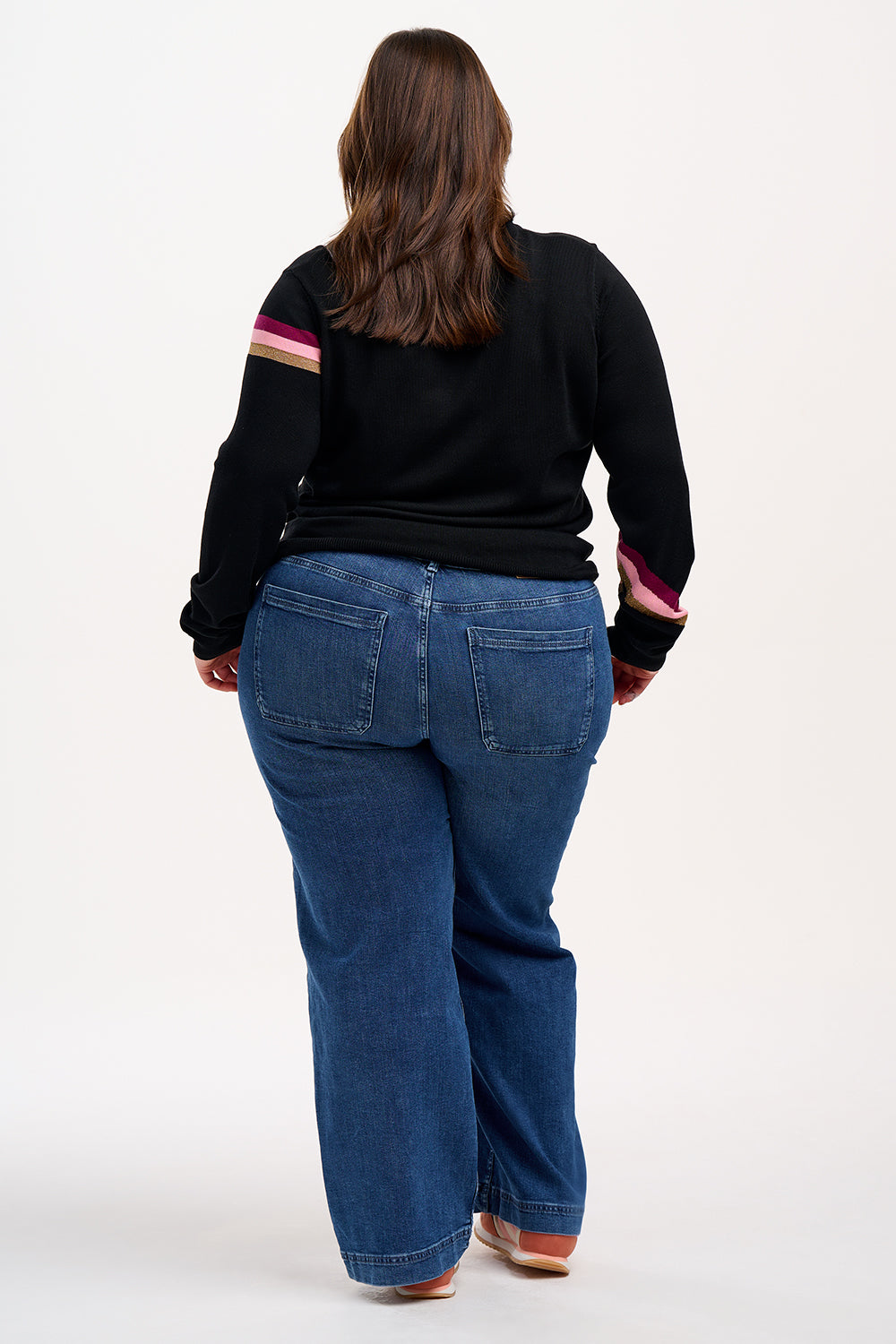 Woman wearing a black sweater with colorful stripes and blue jeans against a white background