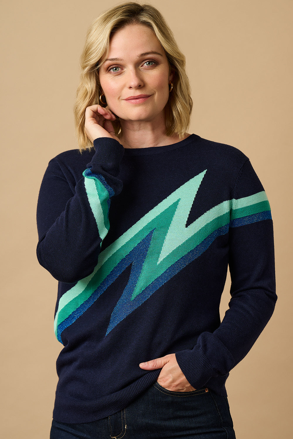 A woman wearing a long sleeve navy jumper with a graphic lightning bolt design in blue and green across the torso and arms.