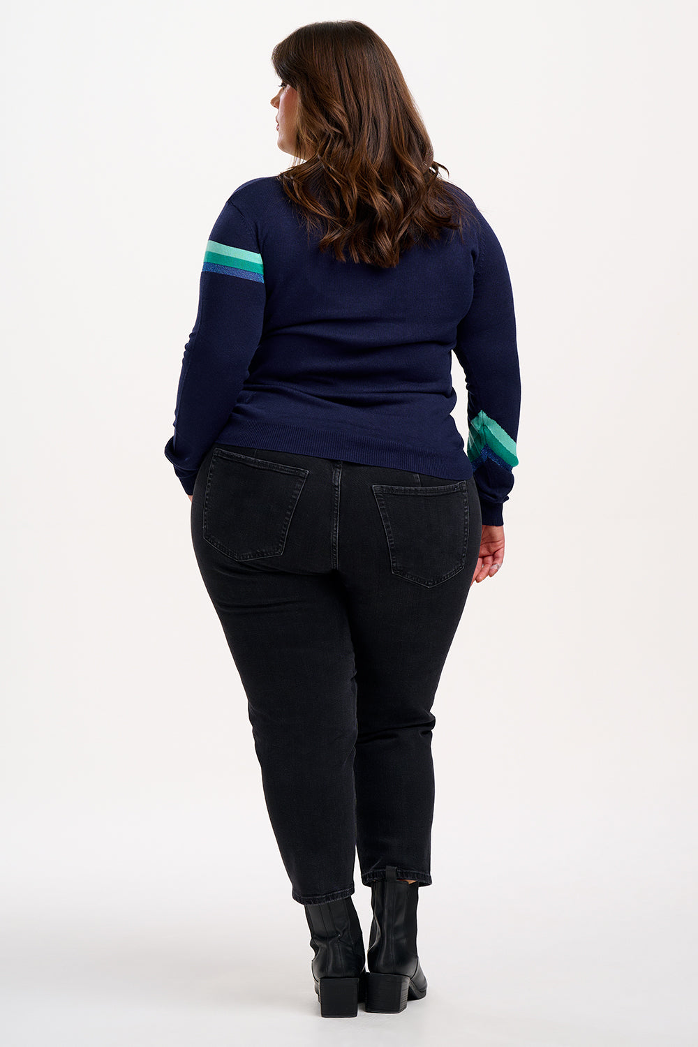 Woman wearing a navy sweater with a green lightning bolt design and blue jeans on a white background