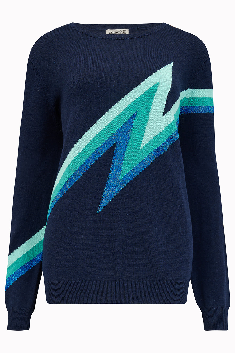 Woman wearing a navy sweater with a green lightning bolt design and blue jeans on a white background