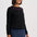 A woman wearing a black long-sleeve knit sweater with pink lightning-bolt embroidery around the neckline, paired with a blue denim skirt, against a light gray studio background.