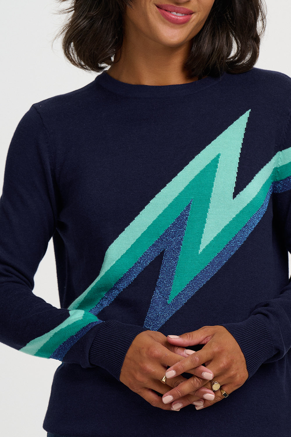 A close-up of a woman wearing a navy blue crewneck sweater with a large textured lightning bolt graphic in shades of green and blue across the chest.