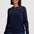 A woman wearing a dark navy blue knit sweater with small embroidered stars in pink, yellow, and blue around the neckline, paired with dark blue jeans, against a light gray studio background.