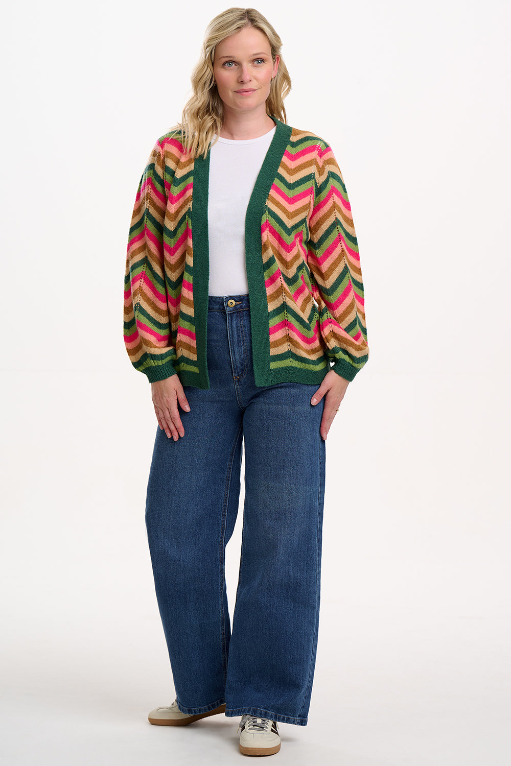 Sugarhill Brighotn model wearing a colorful zigzag patterned cardigan and blue jeans on a white background