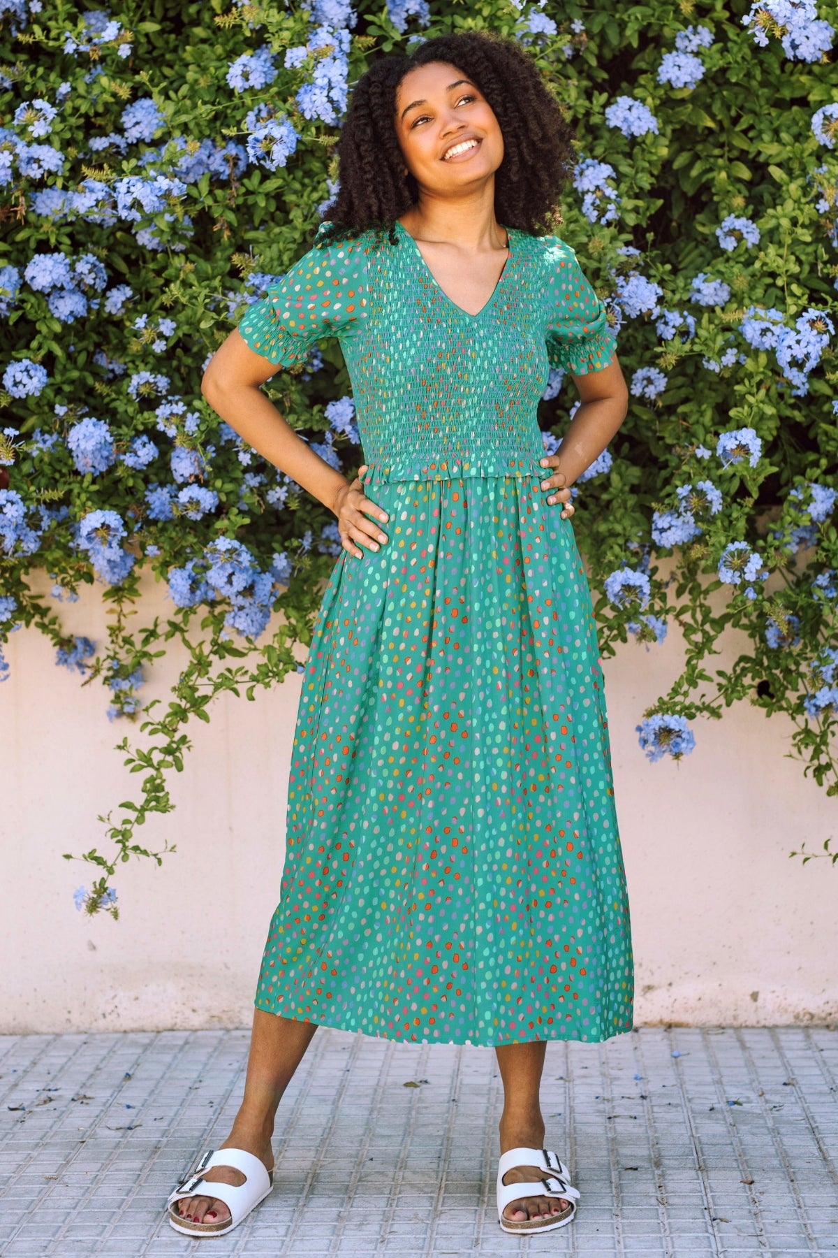 Woman in a green dress standing in front of a floral wall.