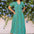 Woman in a green dress standing in front of a floral wall.