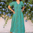 Woman in a green dress standing in front of a floral wall.