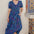A model wearing a midi length dress with a shirred bodice, waist frill, and sleeves, featuring a geometric pattern in blue and other colors on a teal background.