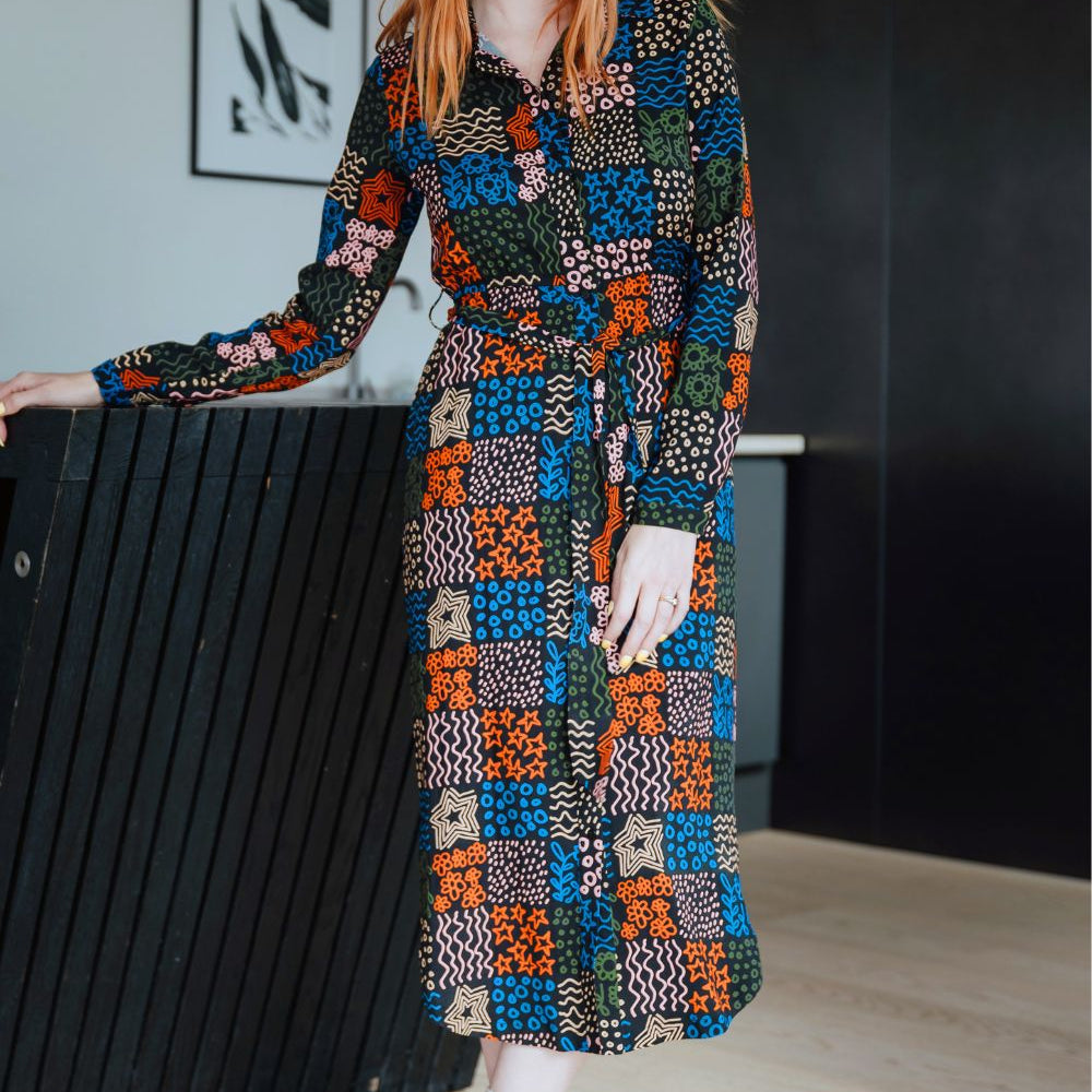 Woman wearing a colorful patterned dress standing indoors.
