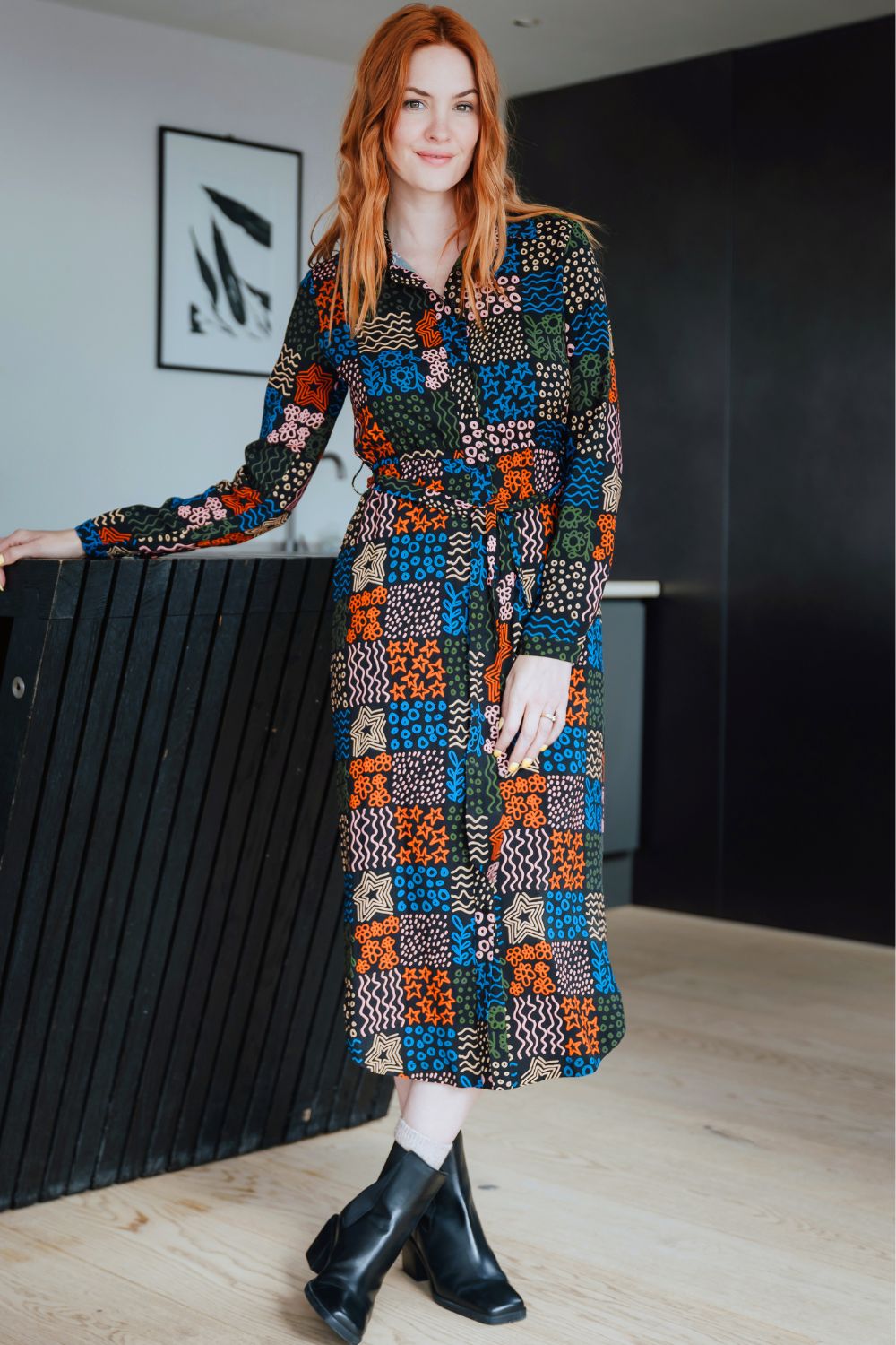 Woman wearing a colorful patterned dress standing indoors.