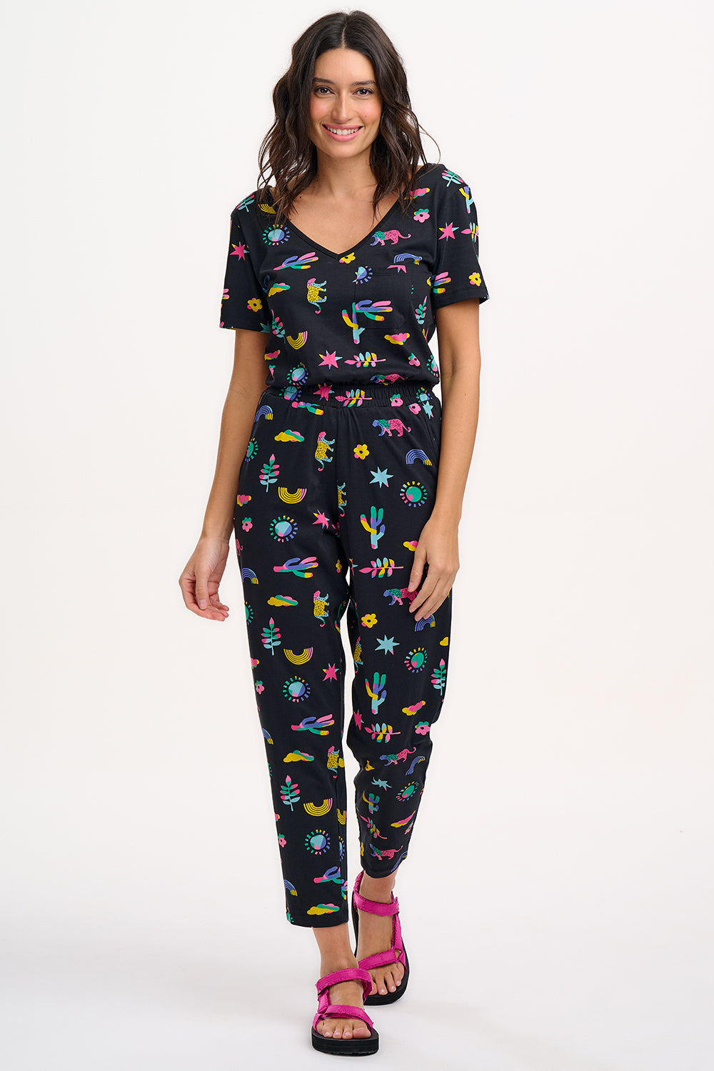 A female model wearing a black cotton jersey jumpsuit with a floral and animal print, featuring short sleeves, a scoop neckline, and elasticated waistband.