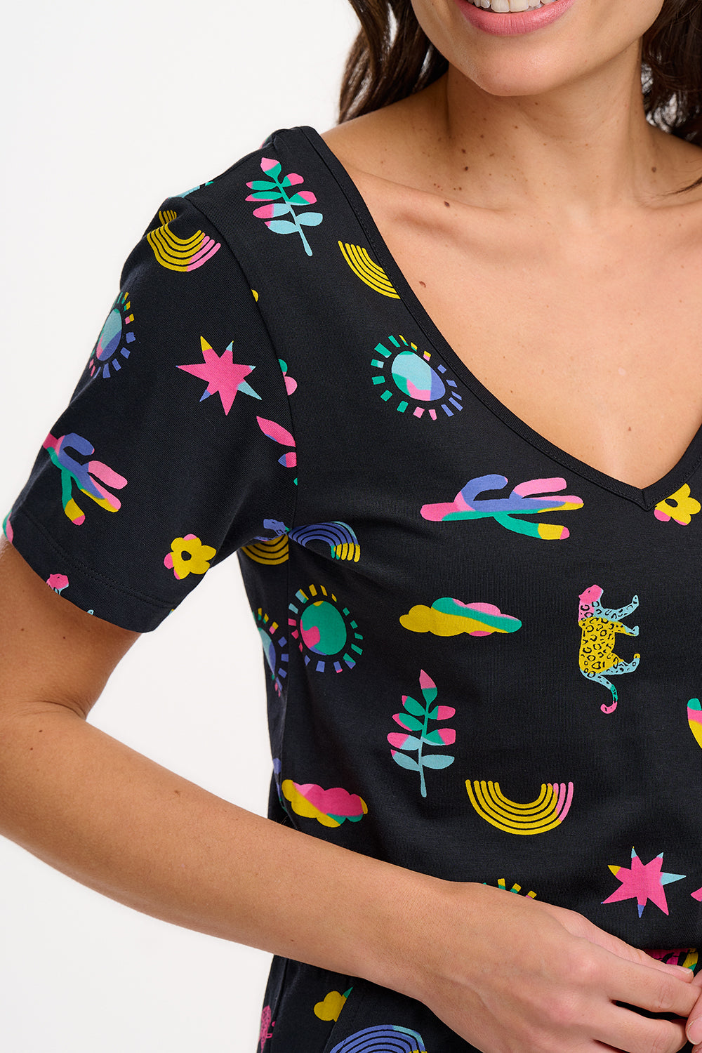 A female model wearing a black cotton jersey jumpsuit with a floral and animal print, featuring short sleeves, a scoop neckline, and elasticated waistband.