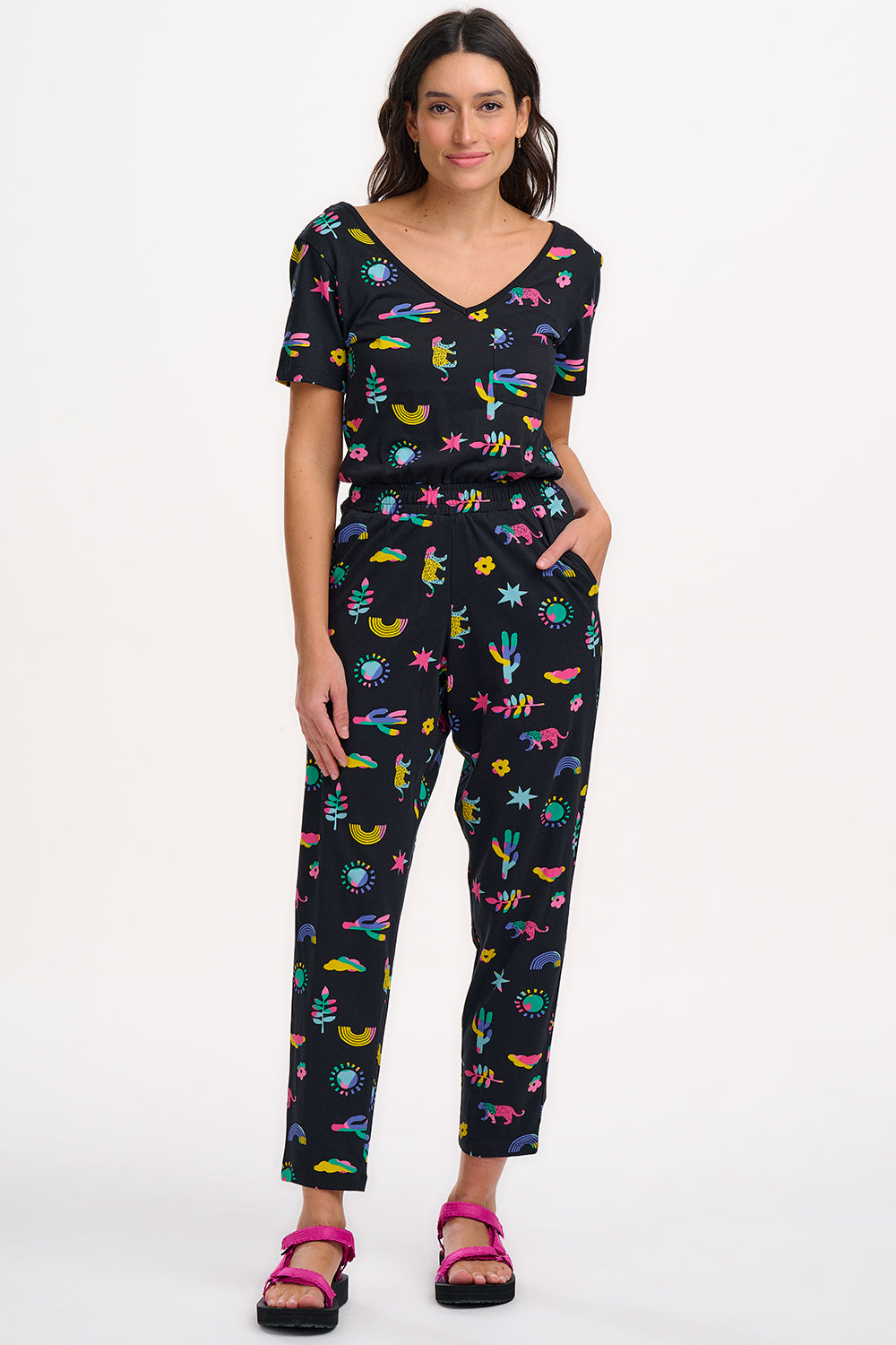 A female model wearing a black cotton jersey jumpsuit with a floral and animal print, featuring short sleeves, a scoop neckline, and elasticated waistband.
