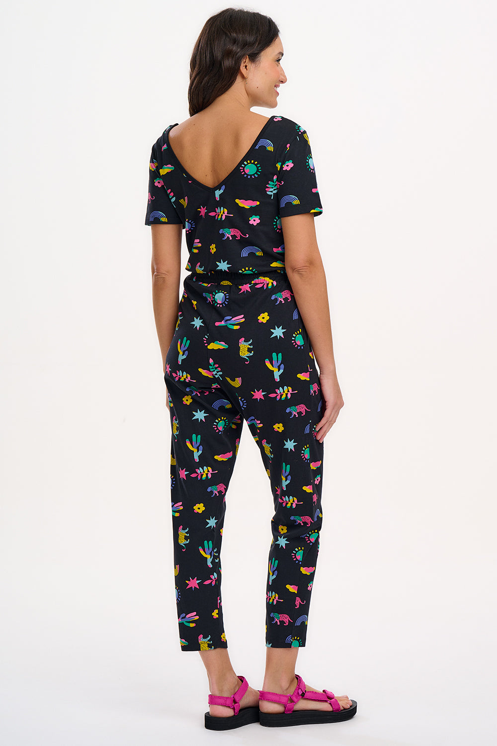 A female model wearing a black cotton jersey jumpsuit with a floral and animal print, featuring short sleeves, a scoop neckline, and elasticated waistband.