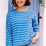 A woman wearing a French blue Breton top with white stripes and a detailed embroidered lobster on the chest, paired with casual jeans.