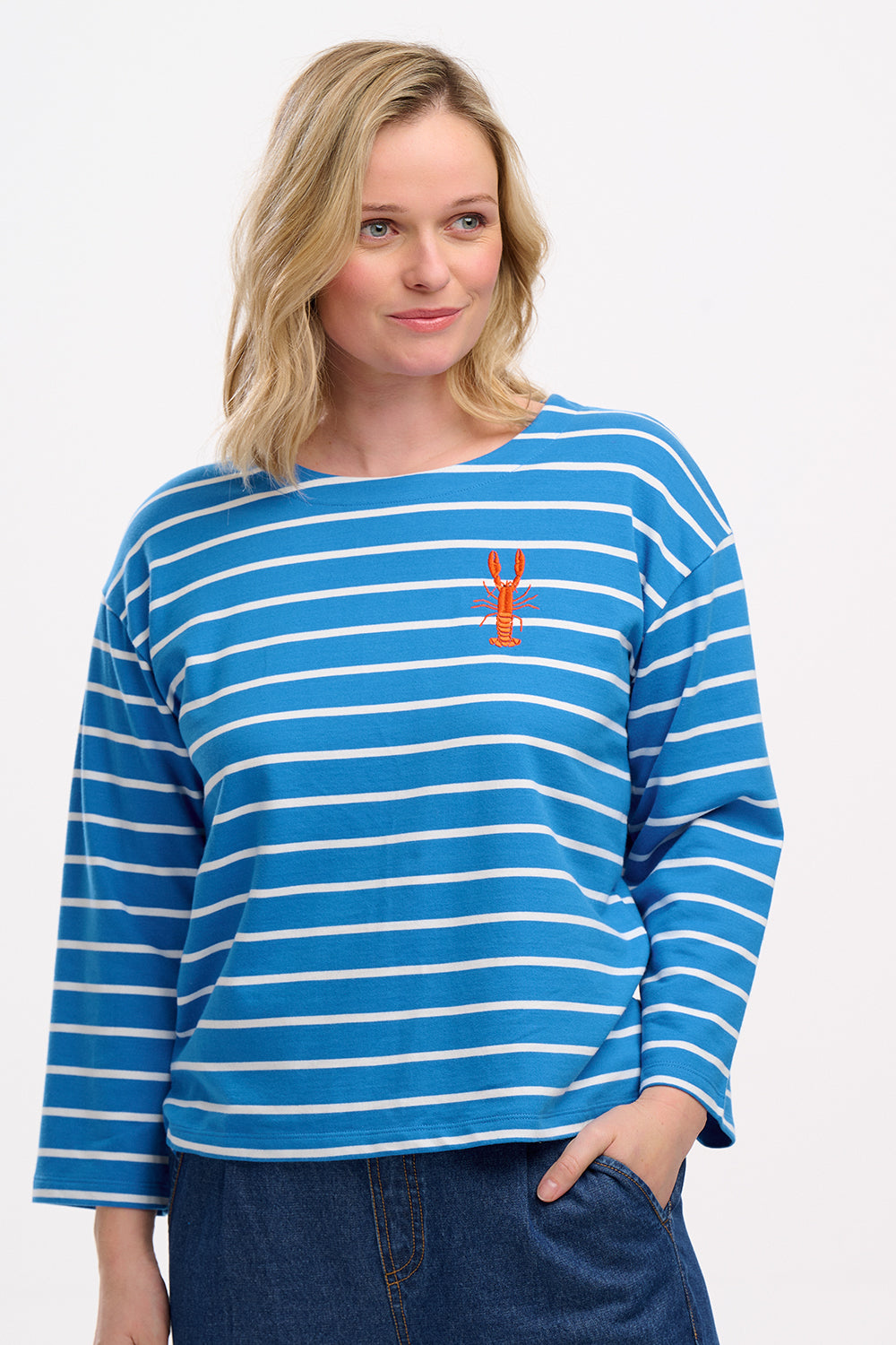 A woman wearing a French blue and lobster stripe Billie Breton top with embroidered lobster on the chest, paired with denim shorts.