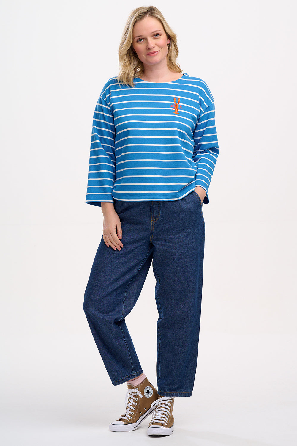 A woman wearing a French blue and lobster stripe Billie Breton top with embroidered lobster on the chest, paired with jeans