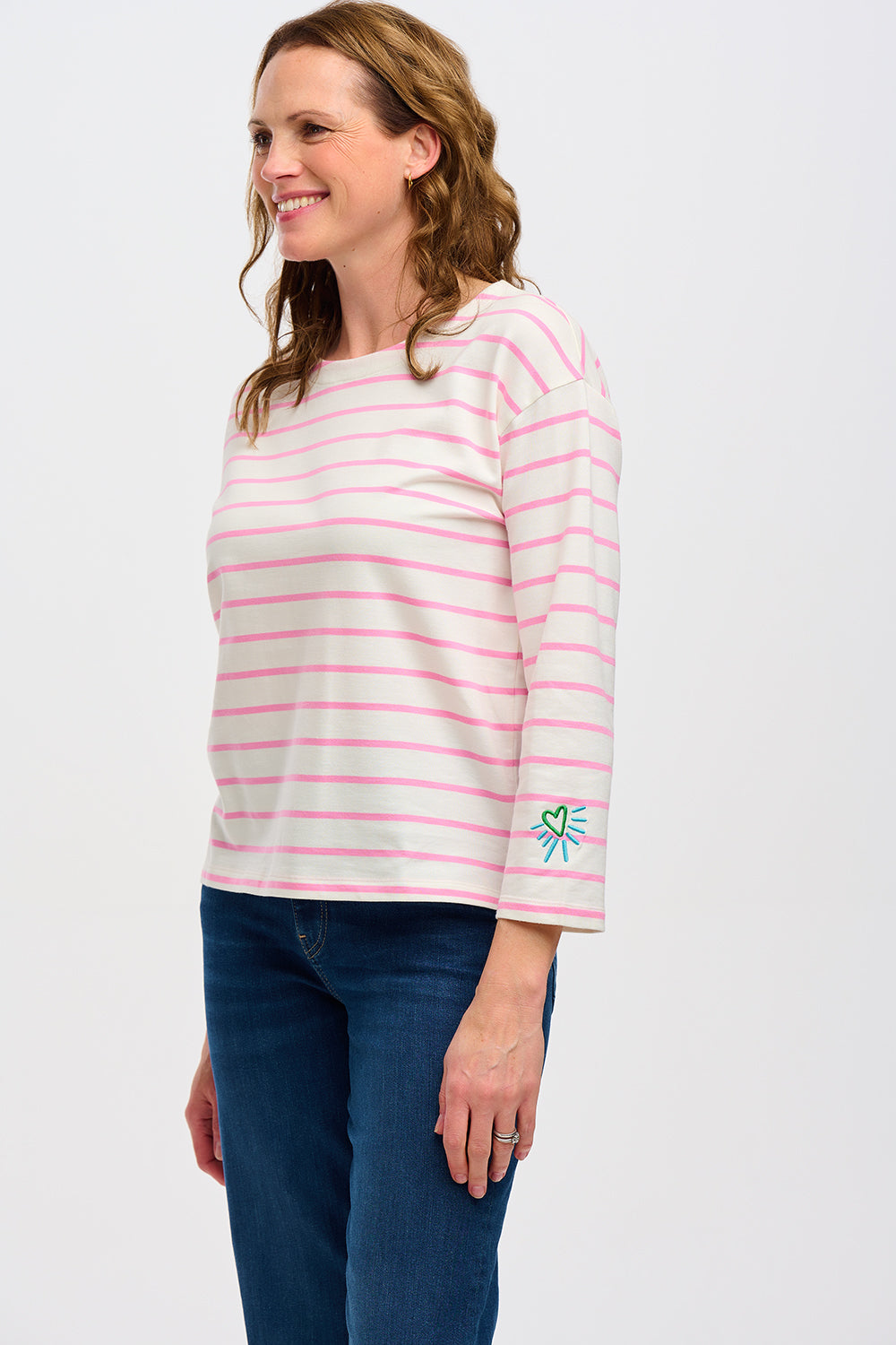 A woman wearing an off-white Breton top with thin pink stripes and a heart design on the sleeve.