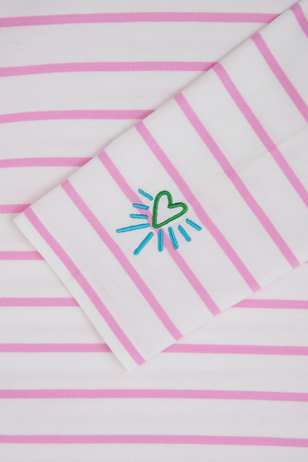 A woman wearing an off-white Breton top with thin pink stripes and a heart design on the sleeve.