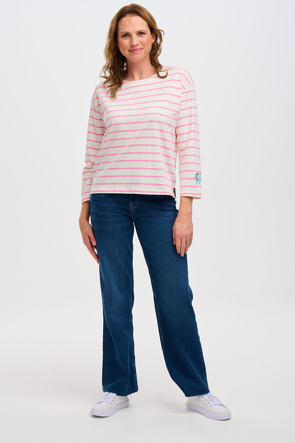 A woman wearing an off-white Breton top with thin pink stripes and a heart design on the sleeve.