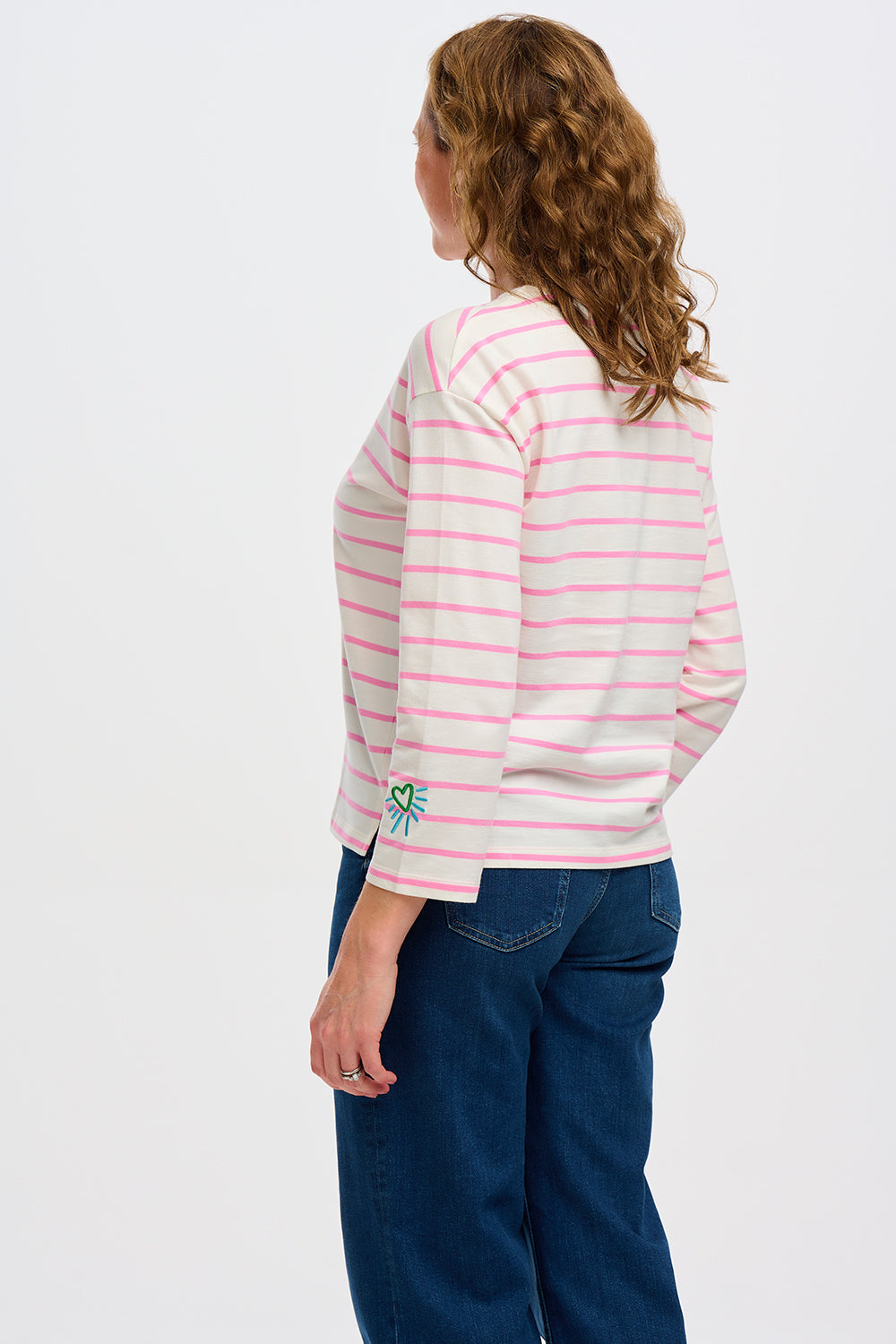 A woman wearing an off-white Breton top with thin pink stripes and a heart design on the sleeve.