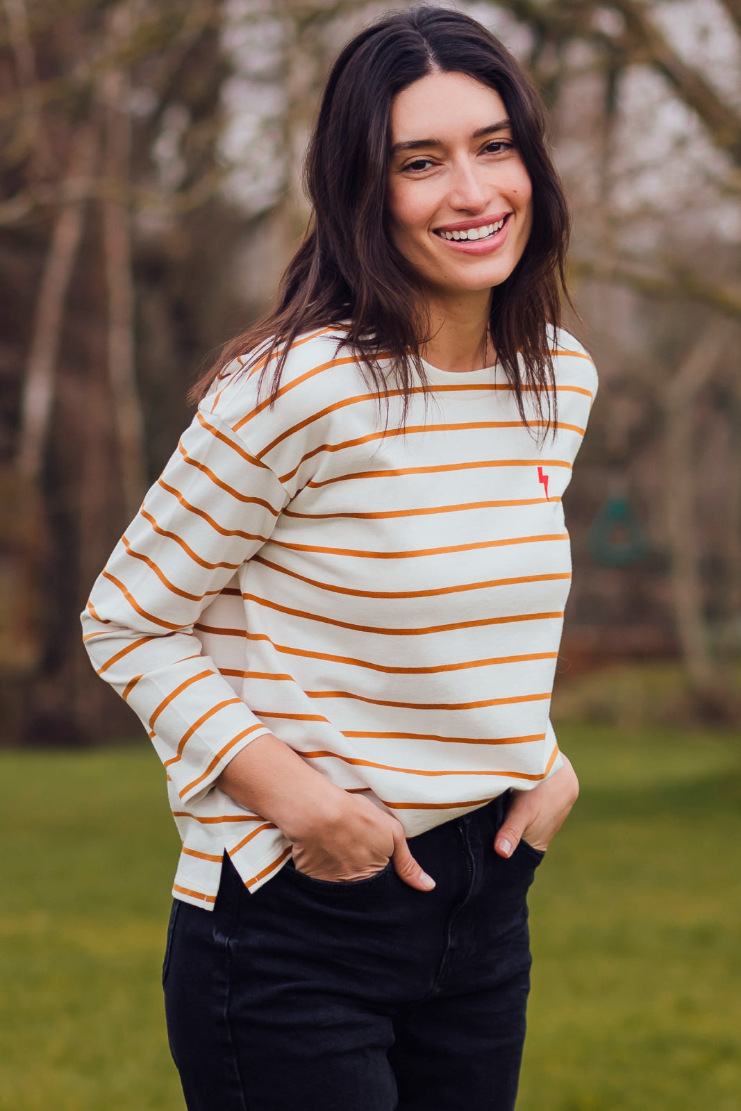 A woman wearing an off-white with thin tan stripes Billie Breton top with a pink embroidered lightning flash on the chest.