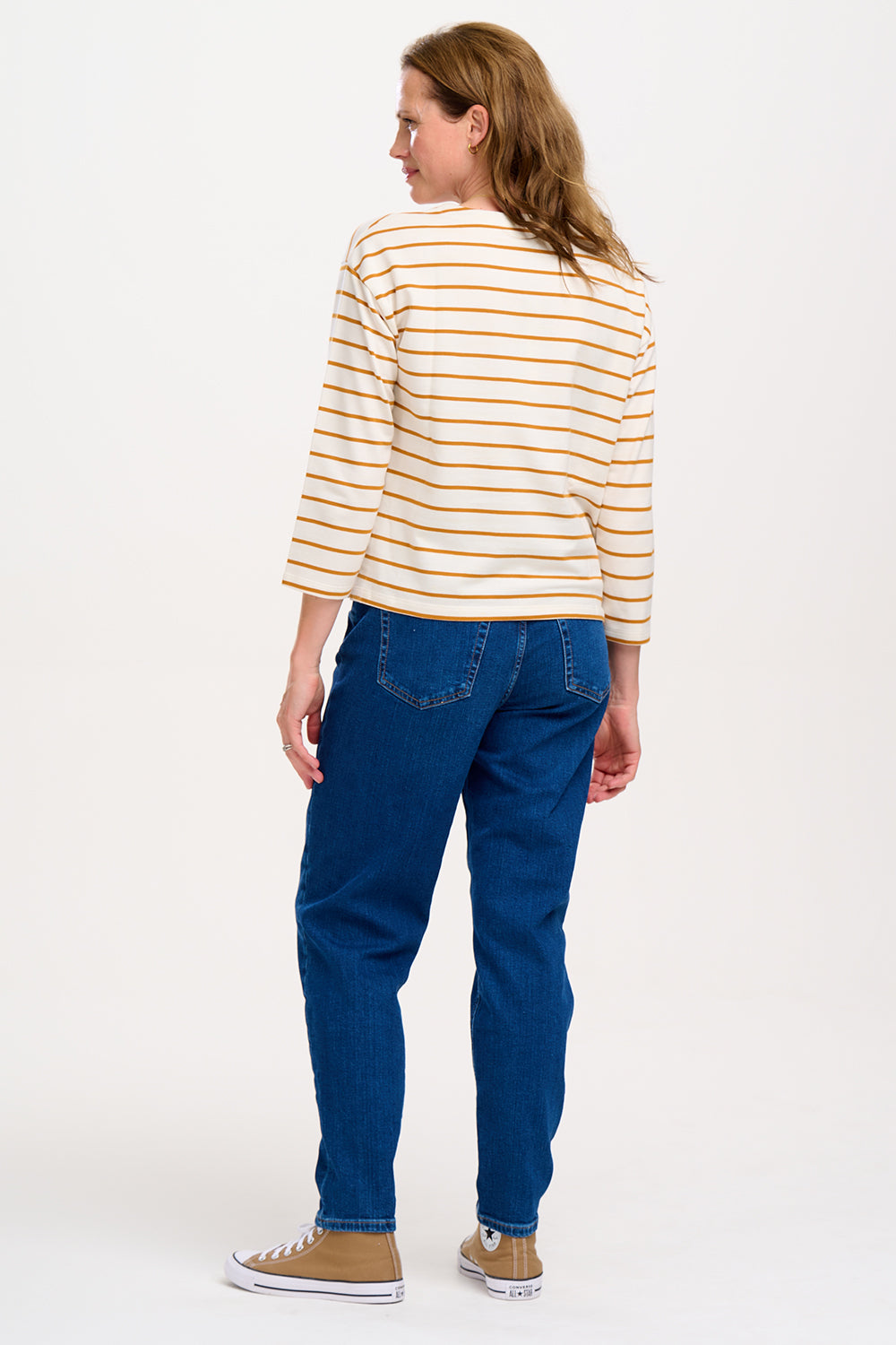 A female model wearing an off-white and tan striped Billie Breton top with a pink embroidered lightning flash on the chest, paired with blue jeans.