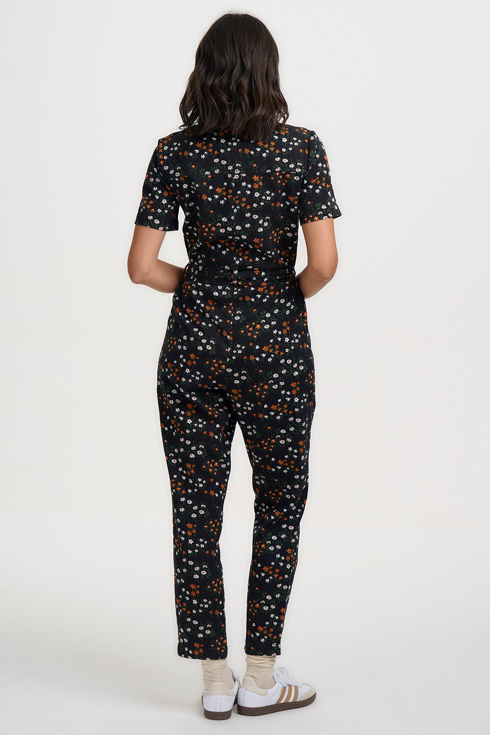 Person wearing a black floral jumpsuit on a white background