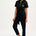 A woman wearing a black boilersuit with a leopard pocket, paired with light-colored sneakers.