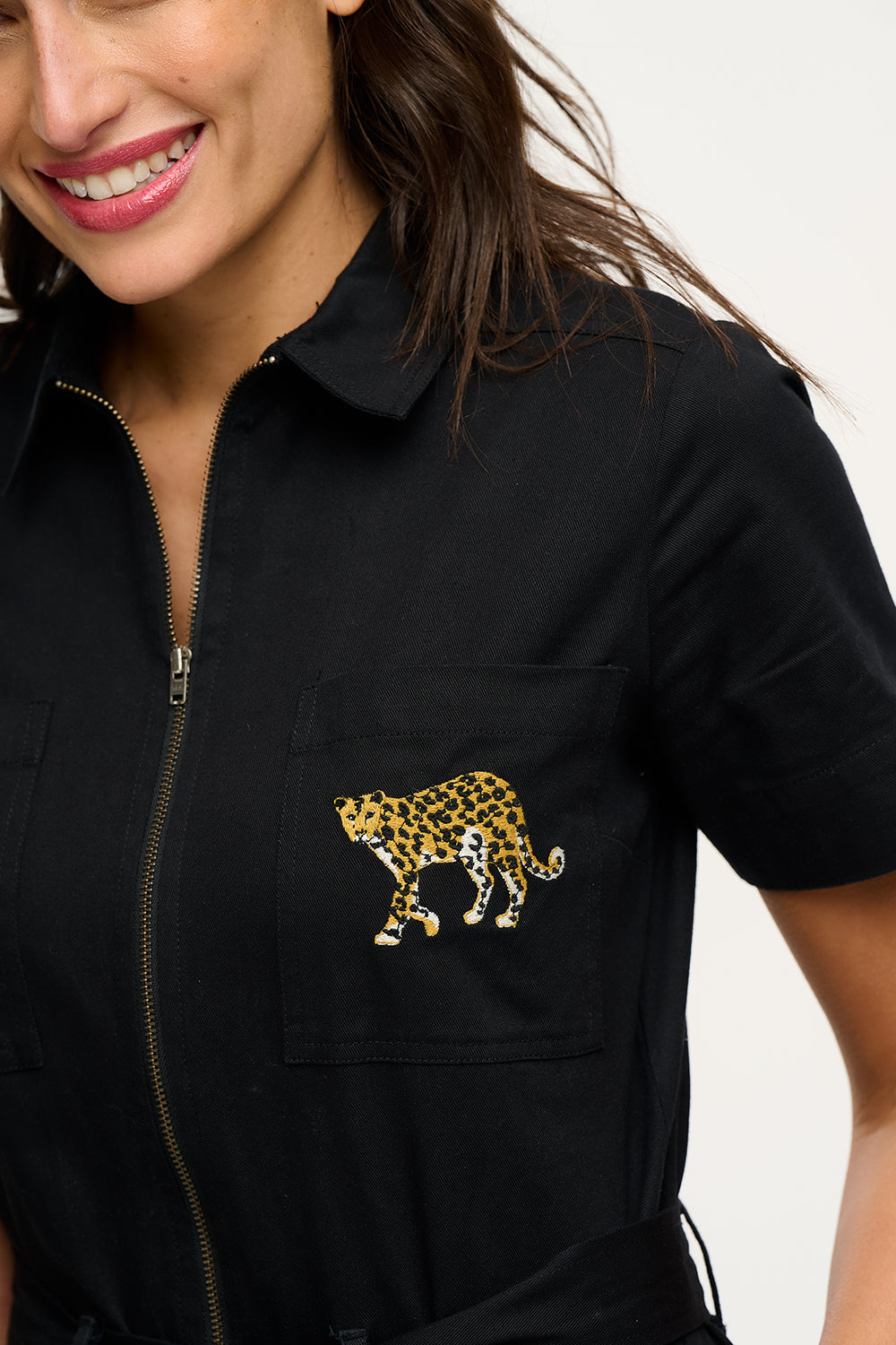 A woman wearing a black boilersuit with a leopard pocket, paired with light-colored sneakers.