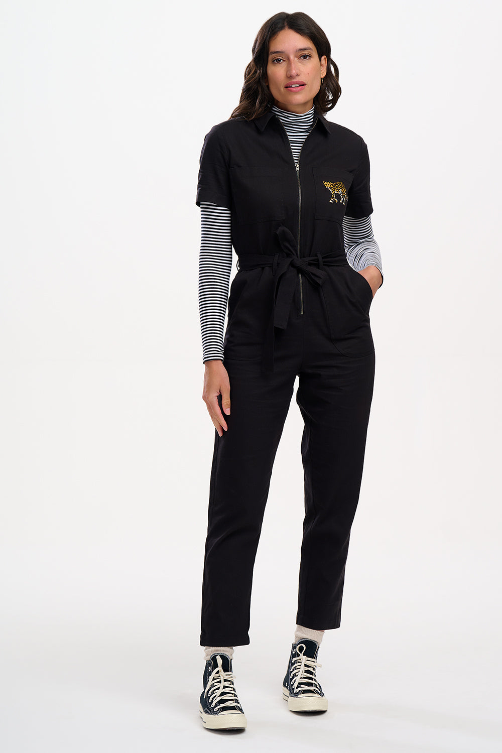 A woman wearing a black boilersuit with a leopard pocket, paired with light-colored sneakers.