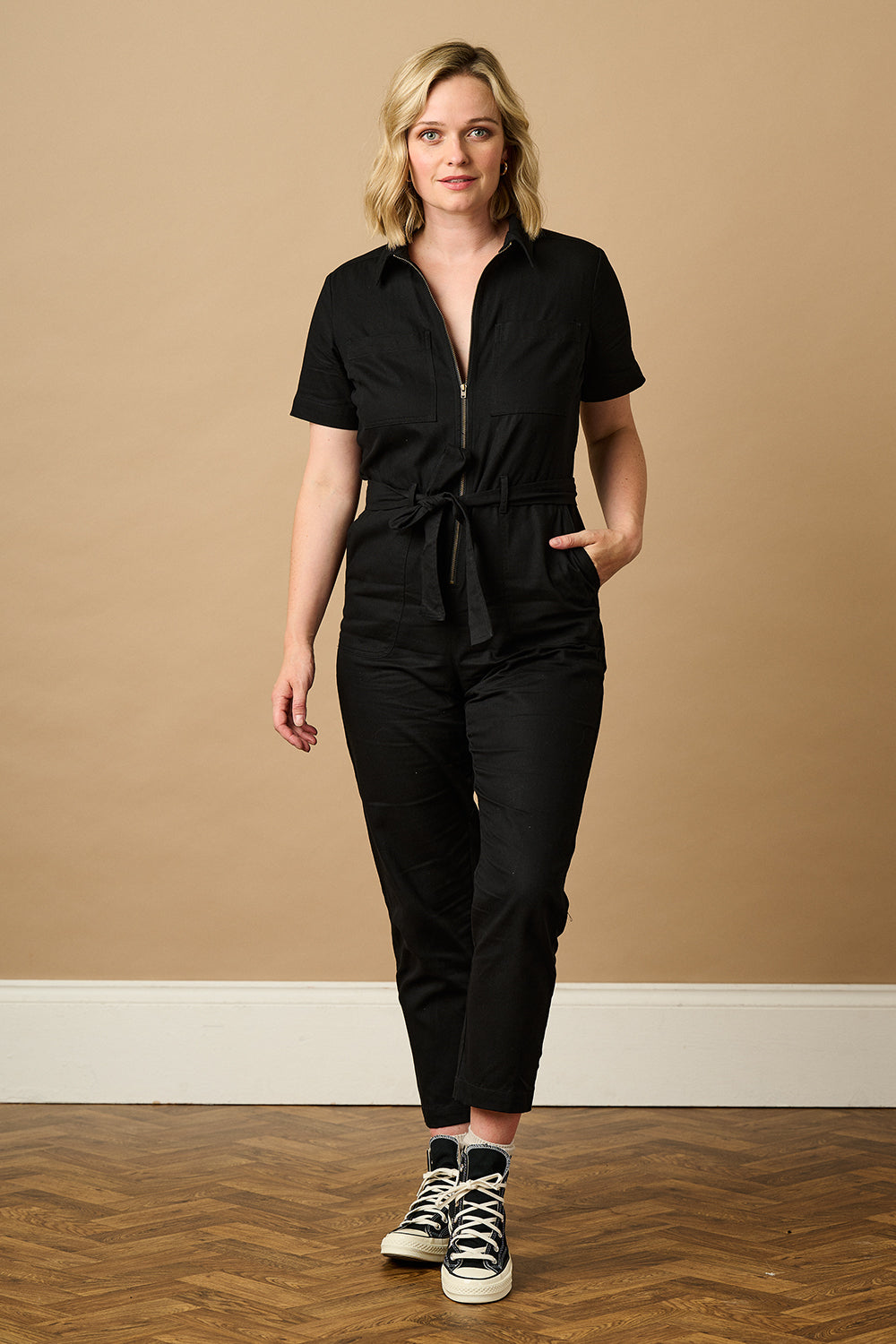 A black boilersuit with outer space-themed embroidery, featuring a planet and stars on the shoulders. The garment has a half sleeve shirt upper, an exposed front zip, and straight legs.