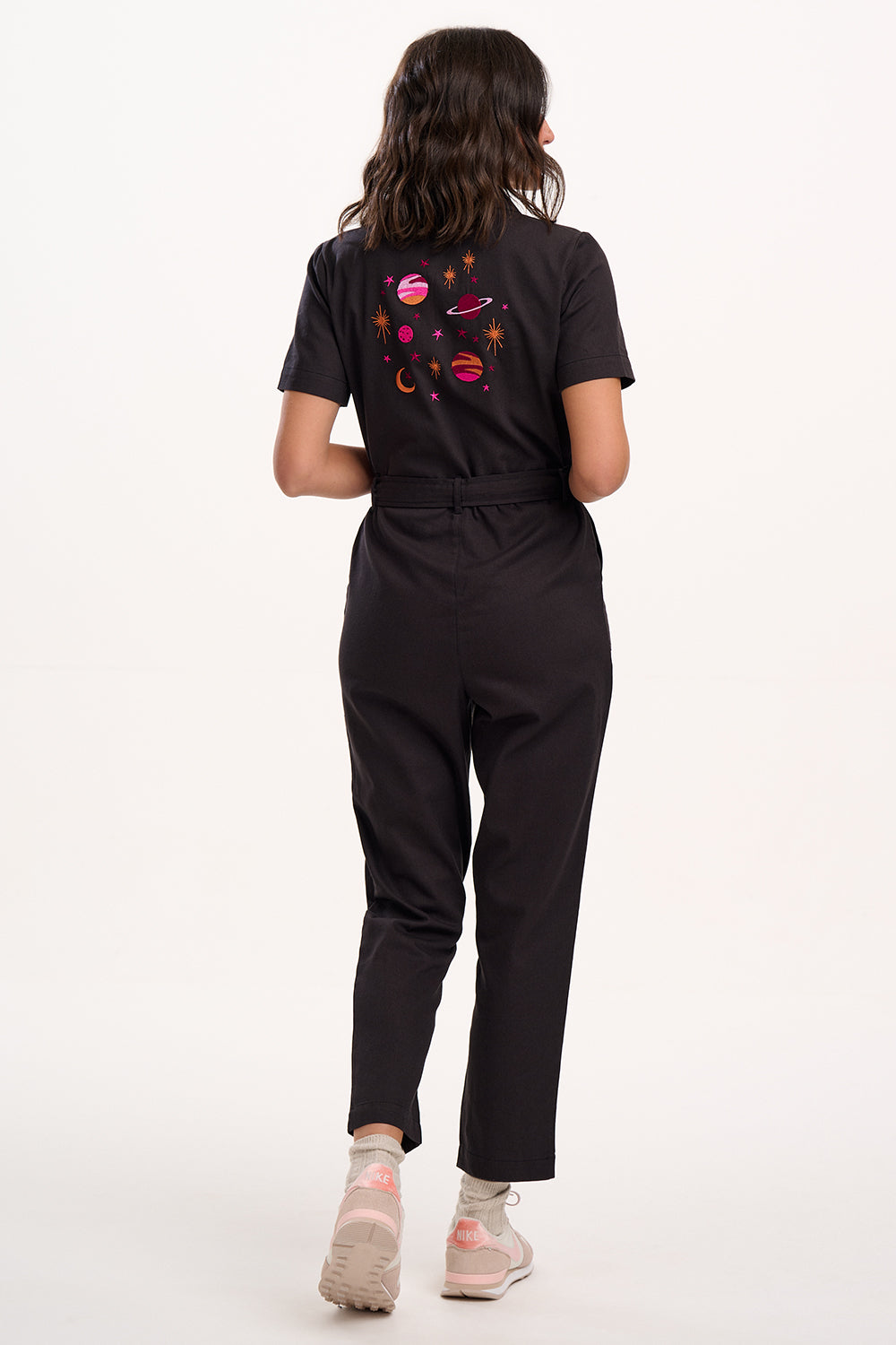 Person wearing a black jumpsuit with colorful designs on the back against a white background