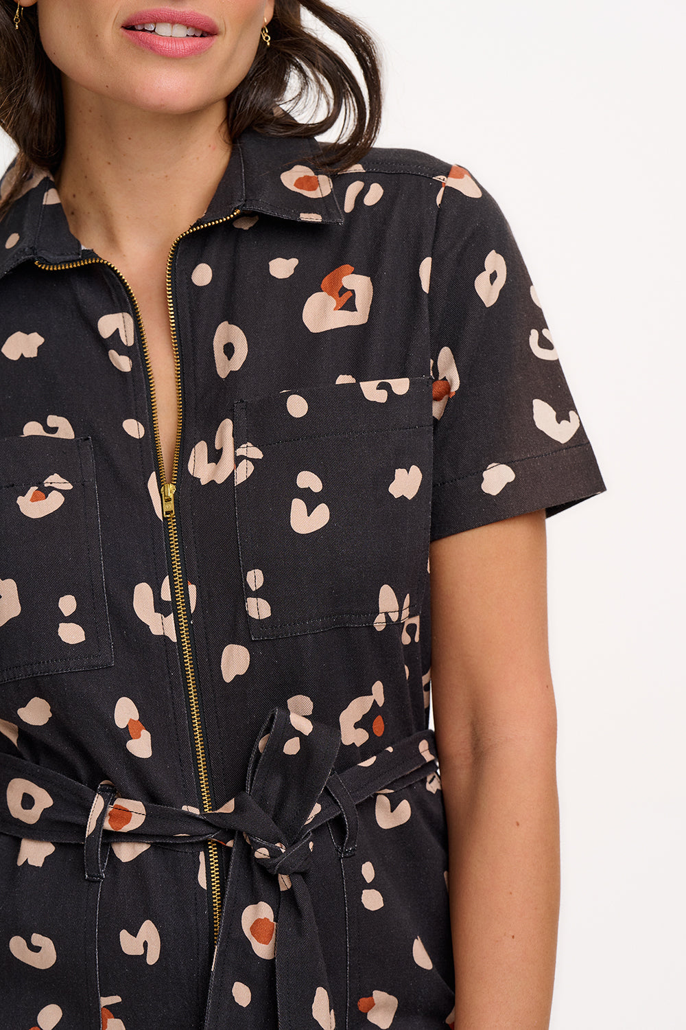 A person wearing a black and tan leopard print boilersuit with a tailored shape, half sleeve shirt upper, and straight legs.