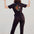 A person standing with their back towards the camera, wearing a black boilersuit with a tiger and floral embroidery on the back. They are making a peace sign with their hands.
