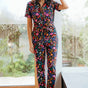 Sugarhill Brighton model wearing a floral jumpsuit, standing in a room with large windows.